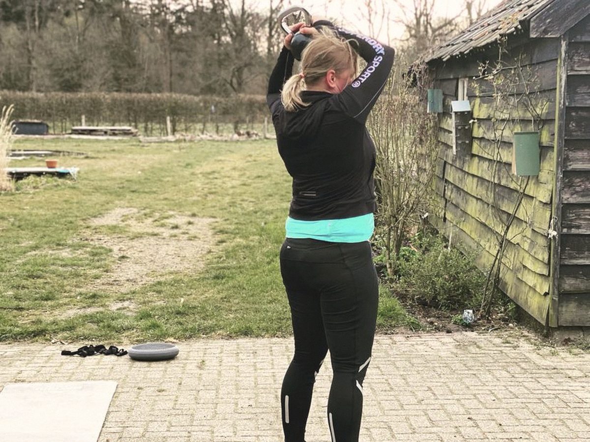 Iemand traint achter het huis met een gewicht boven het hoofd