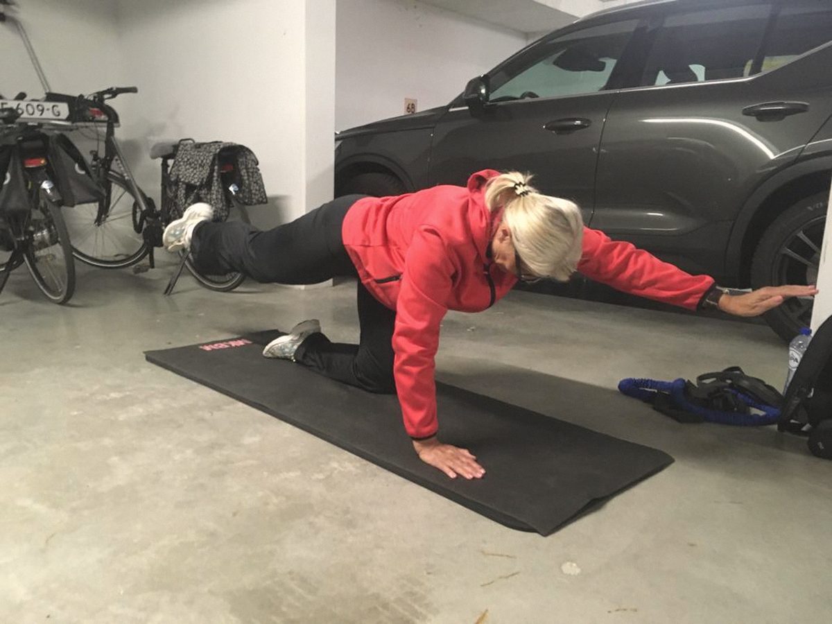 Iemand traint op een mat in een garage naast de auto