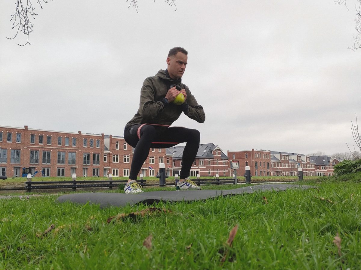 Iemand doet een kniebuiging met een kettlebell bij de huizen