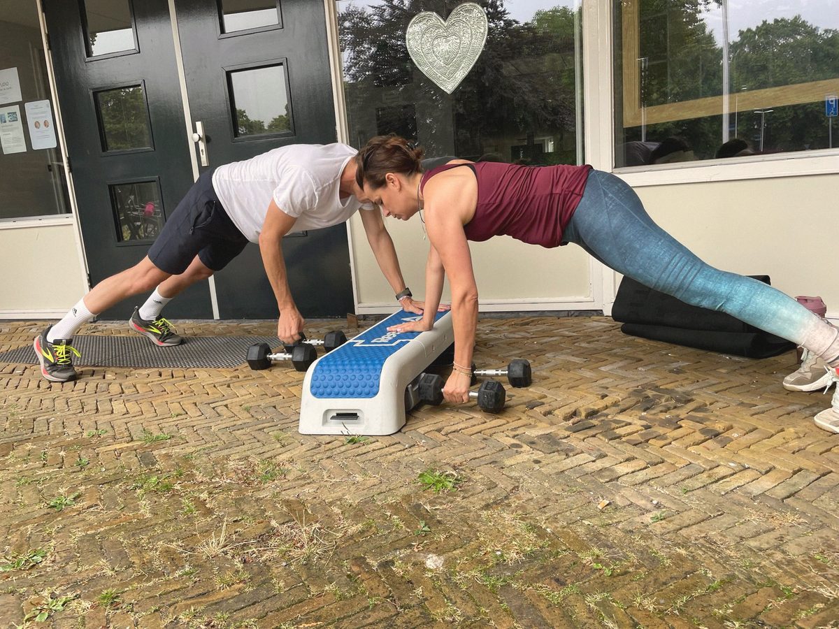 Twee mensen trainen met een opstapje en gewichten voor een voordeur